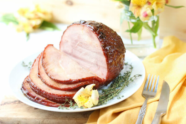 Finished peach honey white wine glazed Easter ham on a serving platter, golden and caramelized, surrounded by fresh thyme