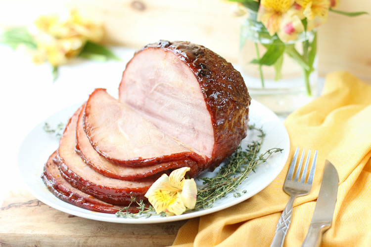 Finished peach honey white wine glazed Easter ham on a serving platter, golden and caramelized, surrounded by fresh thyme